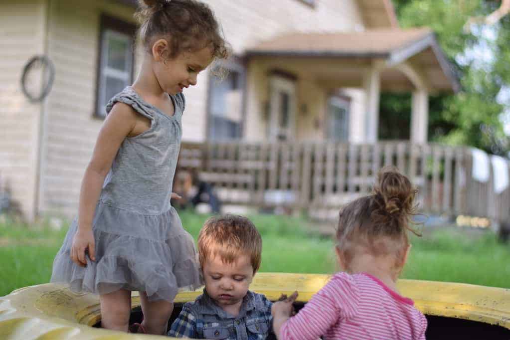 three children playing outside in a sandbox