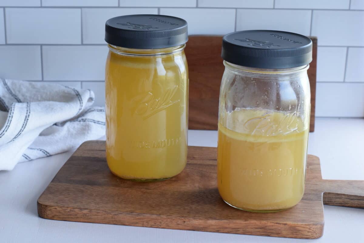 mason jars with leakproof lids and filled with bone broth resting on a wooden cutting board on the countertop.