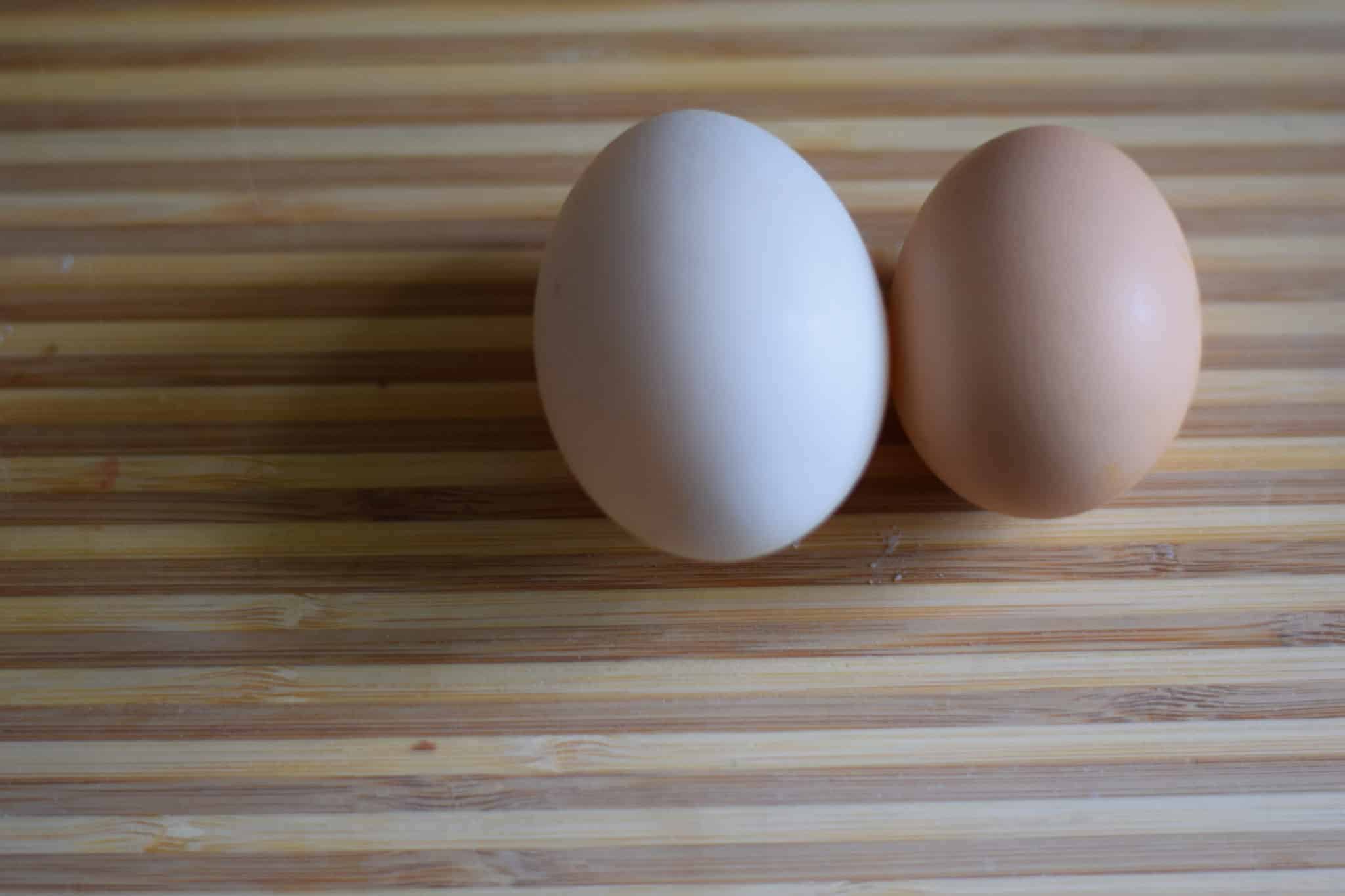 duck egg next to a chicken egg on a wooden cutting board