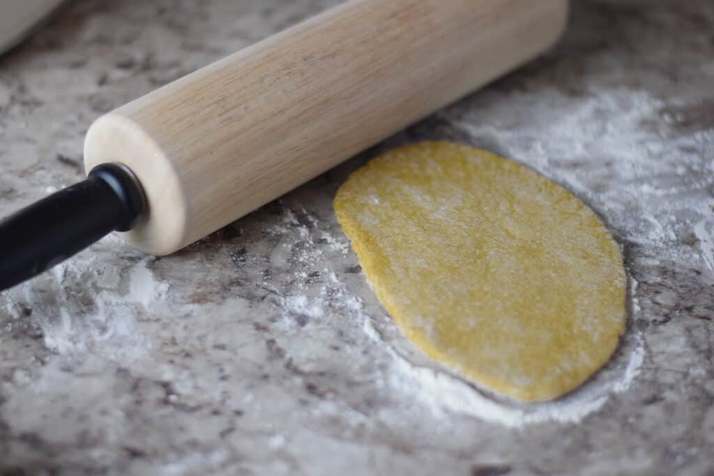 pasta dough rolling out on countertop with a wooden rolling pin