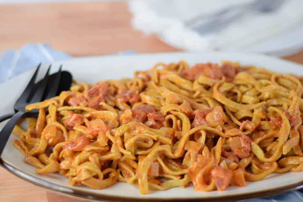 cooked homemade pasta noodles with a creamy pomodoro sauce on a white platter with black utensils