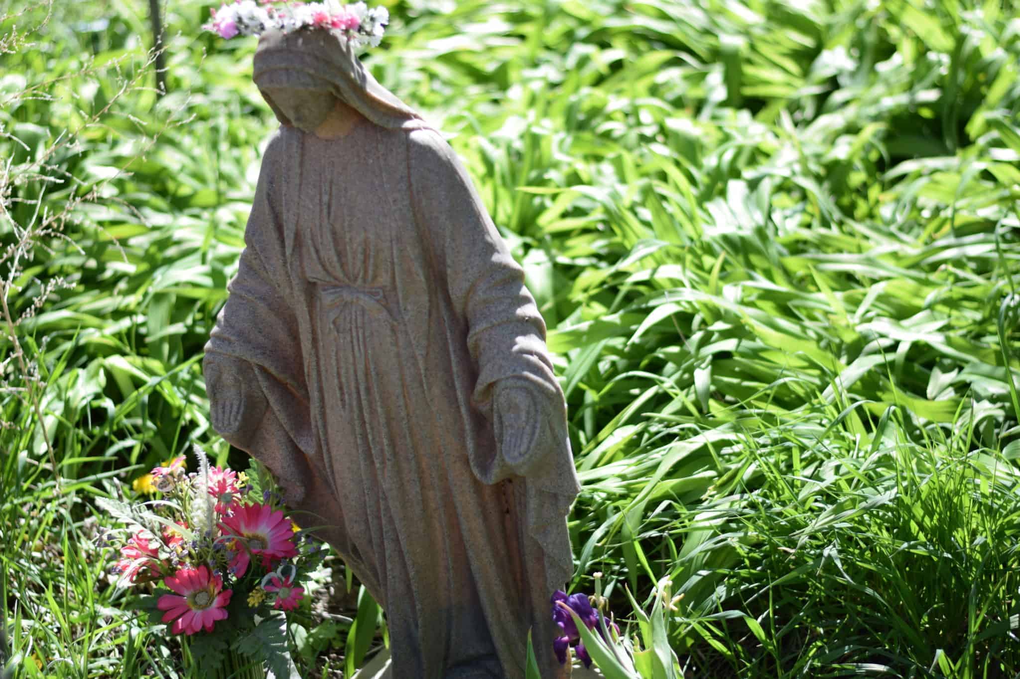 Mary garden shrine for the month of May is decorated with flowers and she is wearing a floral crown