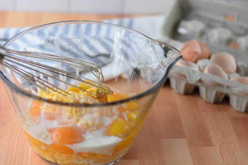 mixing the eggs, cream, and cheddar cheese in glass bowl