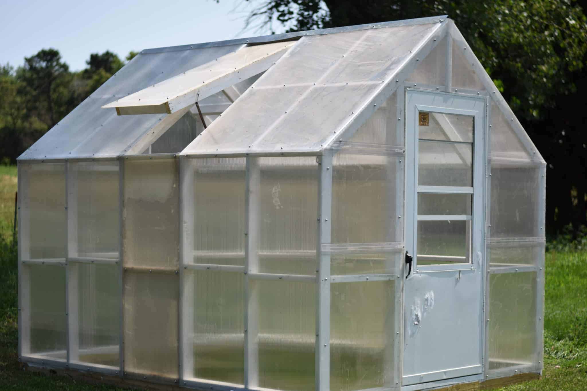 Finished greenhouse outside in the garden with one vent opened on side of roof. 