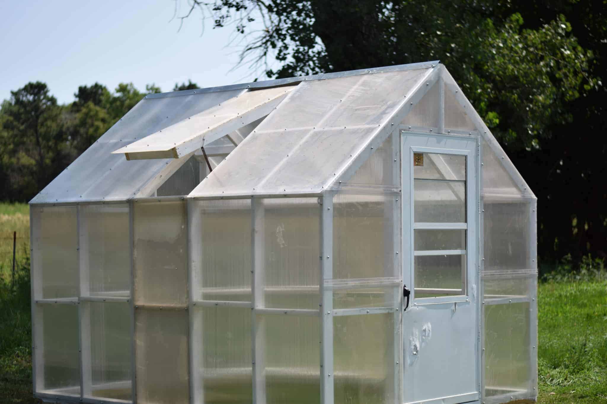 Completed greenhouse in outdoor garden with trees in background. 