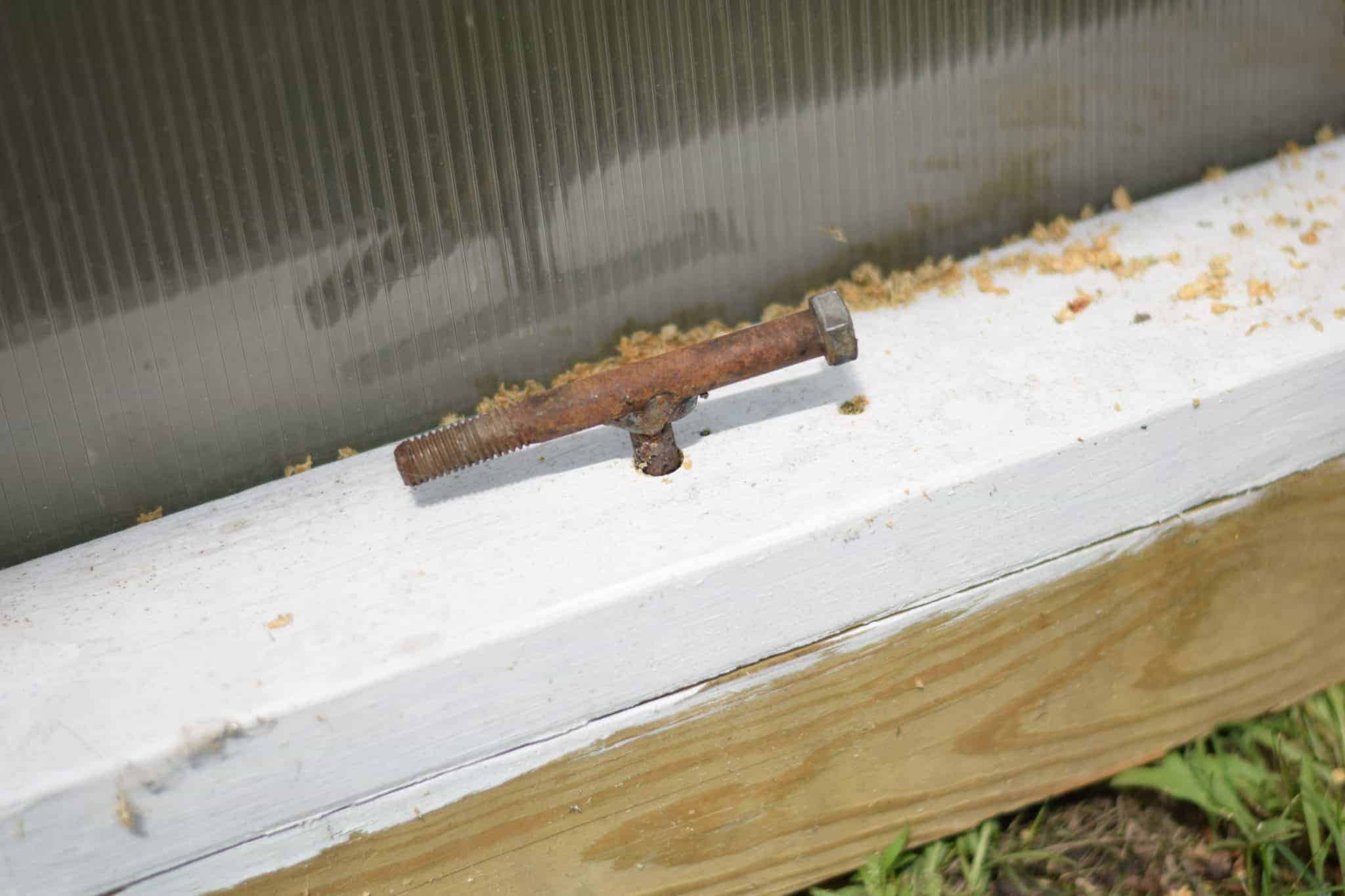 Metal t’s screwed into the bottom frame of the greenhouse and the ground.