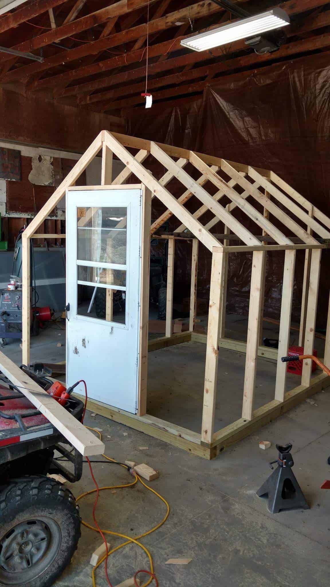 The greenhouse wall frames and roof frame are constructed and the white screen door has been added to the door frame. 