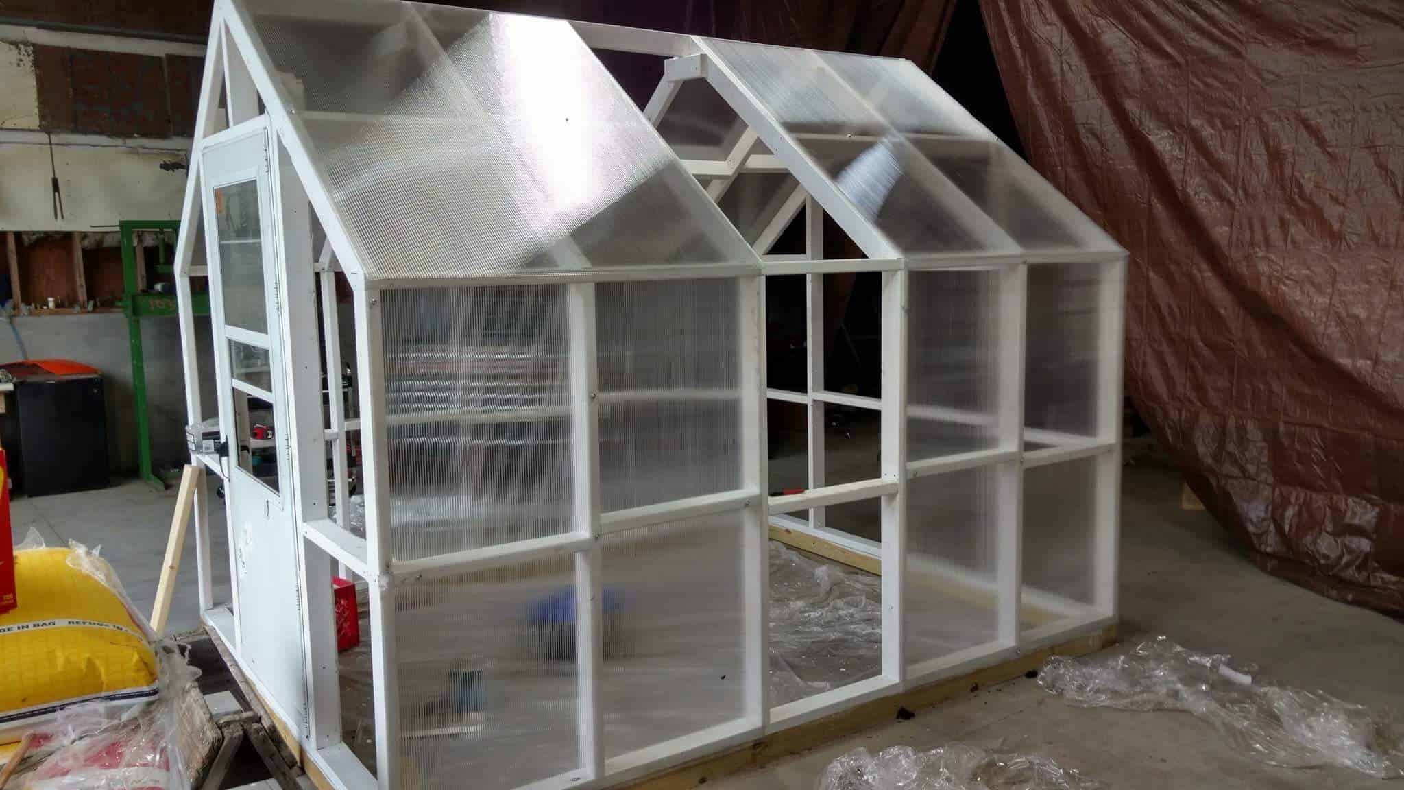 Polycarbonate plastic sheeting is being installed on the greenhouse and the frame has been painted white.