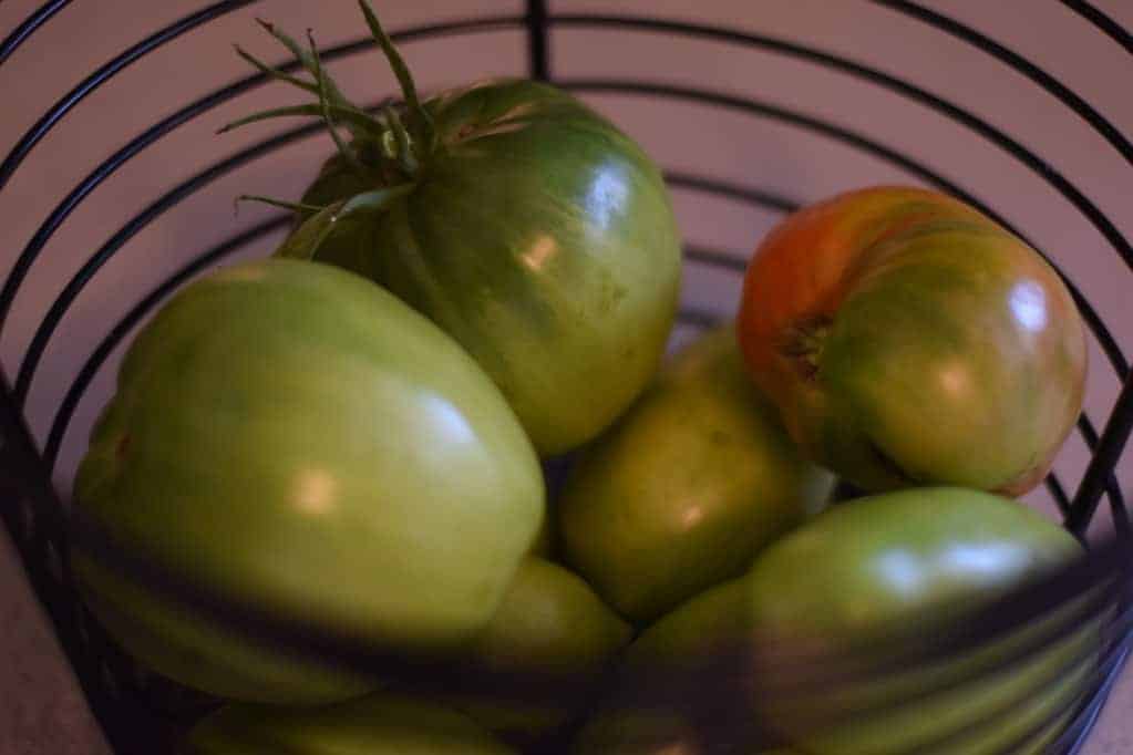 green tomatoes in a black wire basket