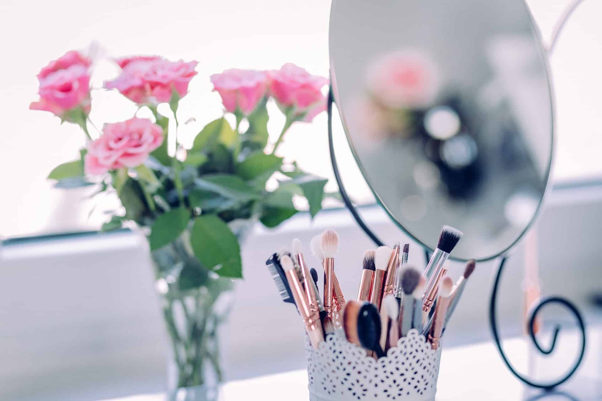 vanity with makeup brushes, mirror, and pink roses in a vase