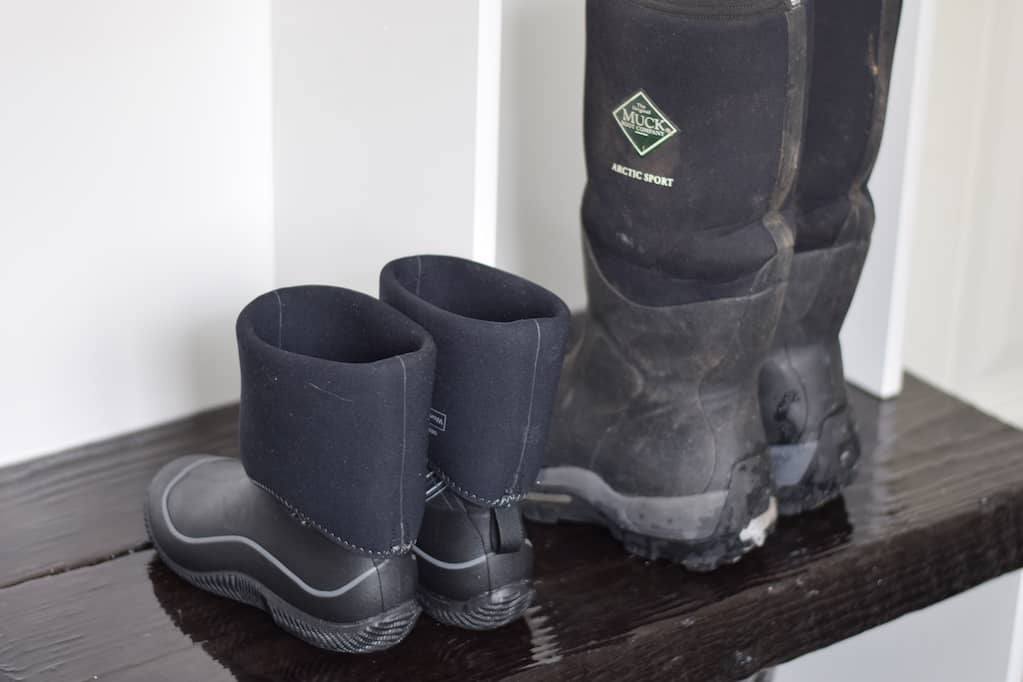 his and her muck boots on a bench in the mudroom