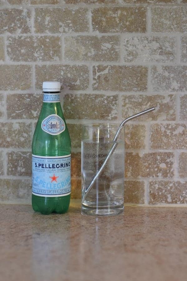 bottle of Pellegrino water with a glass on countertop. 