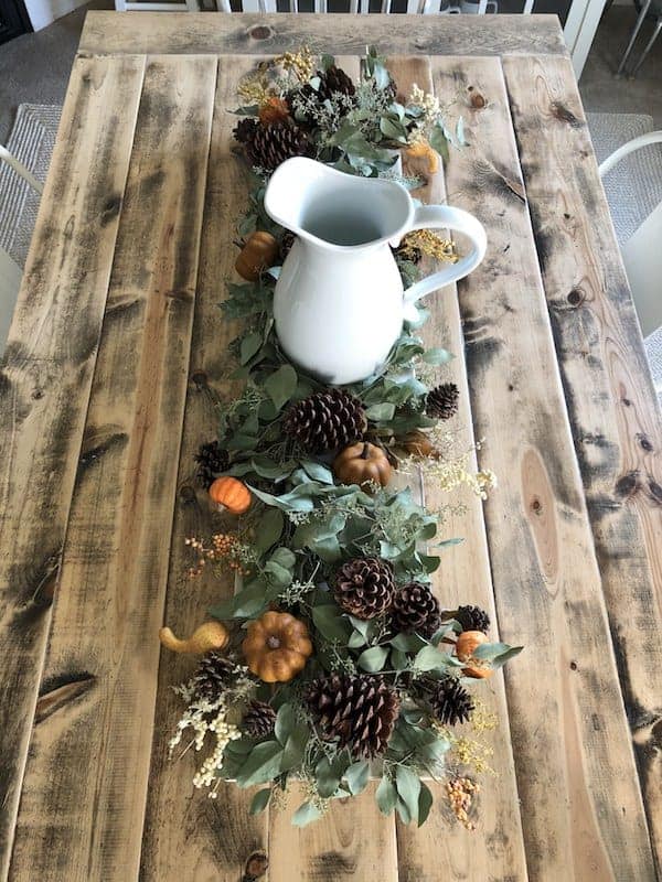 farmhouse table lined with eucalyptus greenery, small pumpkins, and pinecones