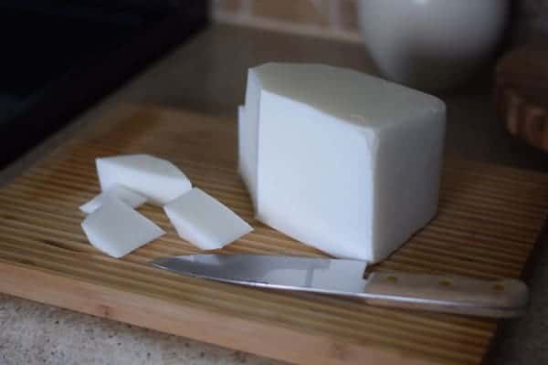 block of goat milk soap base with a large knife on a cutting board