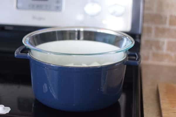 large blue pan on the stove top with a glass pyrex bowl set up on top as a double boiler.