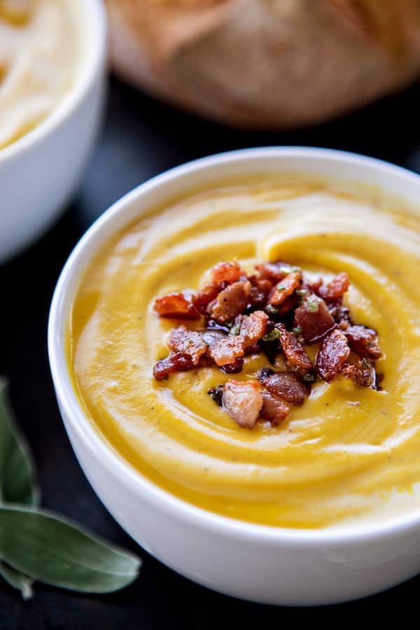 Close up image of roasted butternut squash soup with bacon on top in a white bowl