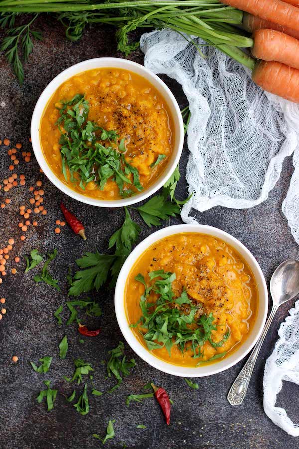birds eye view of two bowls of vegan carrot soup w/ lentils