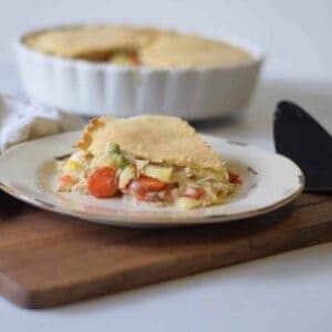 plate with a piece of chicken pot pie in the foreground and the remaining chicken pot pie in a pie dish in background