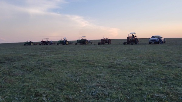 row of tractors lined up at dusk with sunset in a hay field