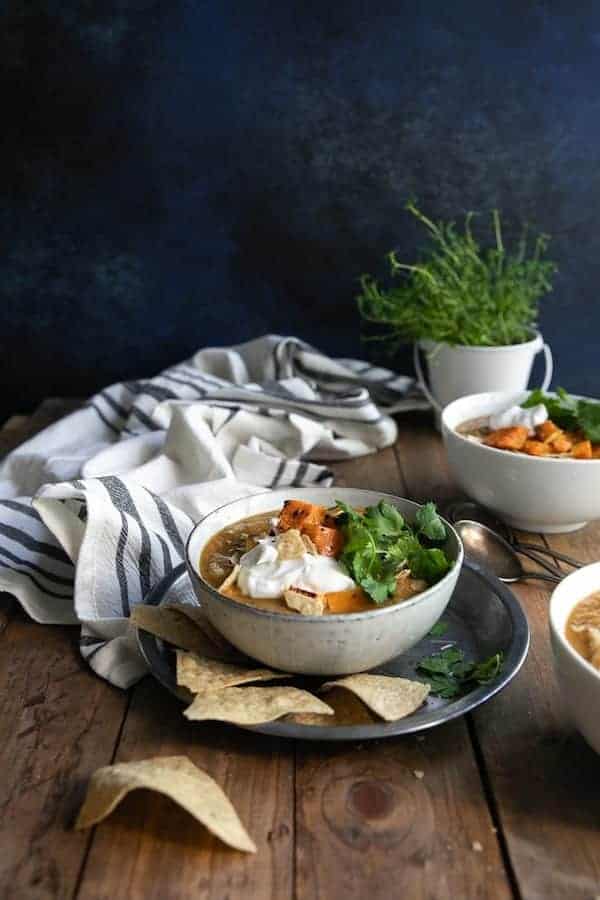 bowls of the squash and black bean soup in white bowls and sitting on a rustic wooden table