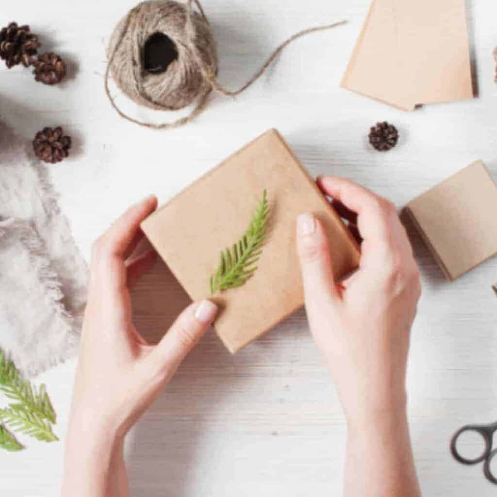 flat lay of brown gift box with twine, pine cones, and green herbs