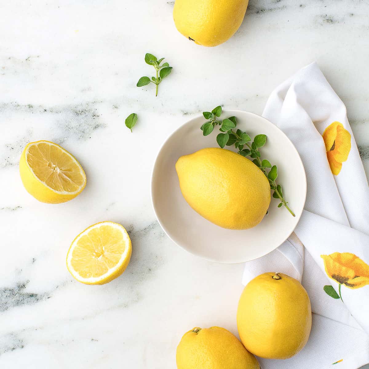 whole lemons and slices of lemon on a countertop with a small white bowl and tea towel.