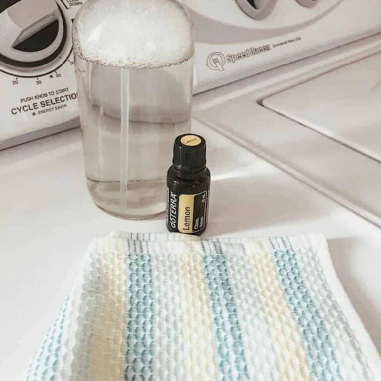 glass spray bottle with a lemon essential oil bottle and cleaning cloth on the washing machine