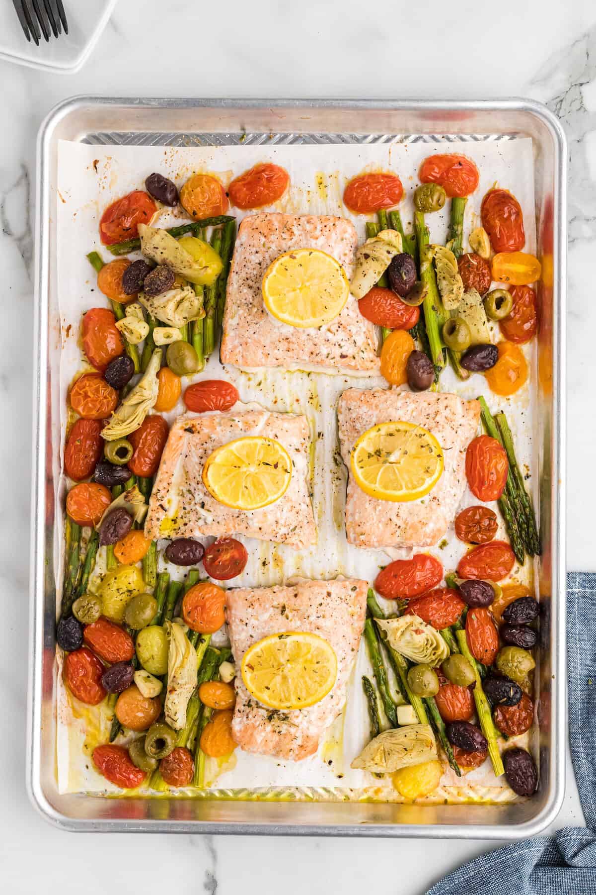 mediterranean salmon recipe on a sheet pan with fresh veggies and lemon slices.