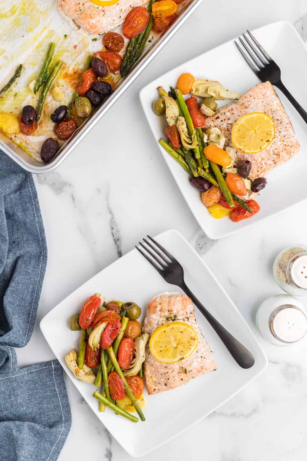 two white square plates with Mediterranean salmon and veggies.