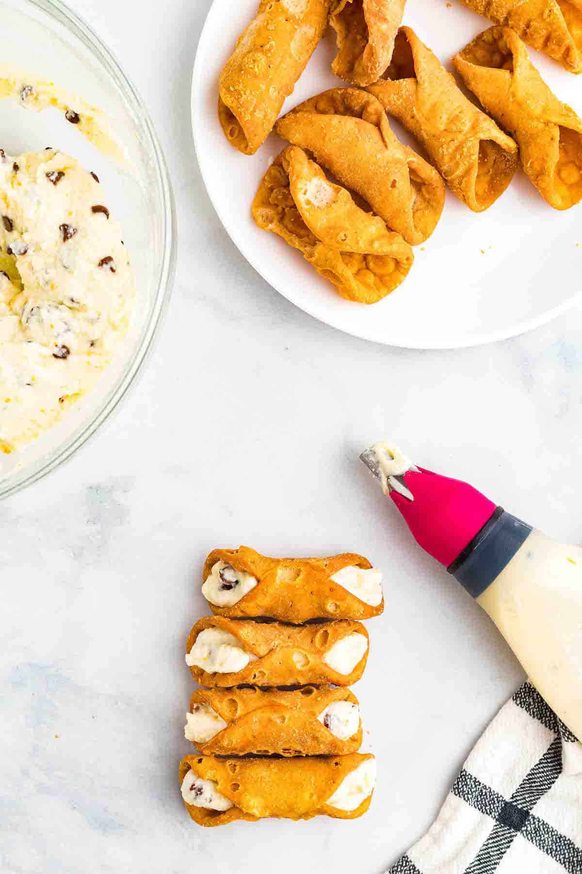 using a pastry bag to fill the cannoli shells.