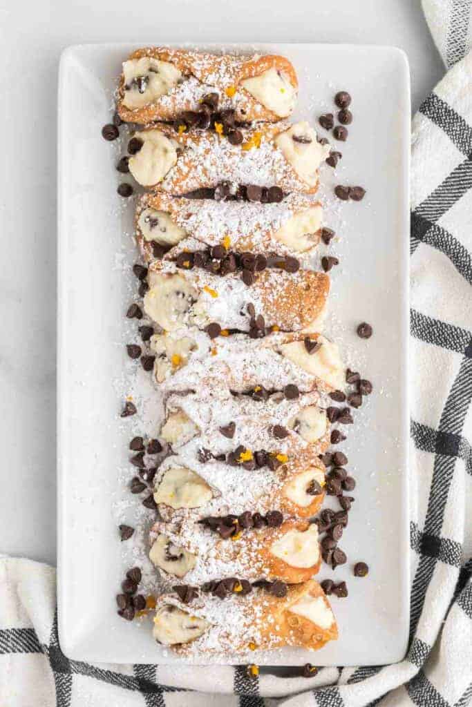white tray with cannolis and topped with powdered sugar and chocolate chips
