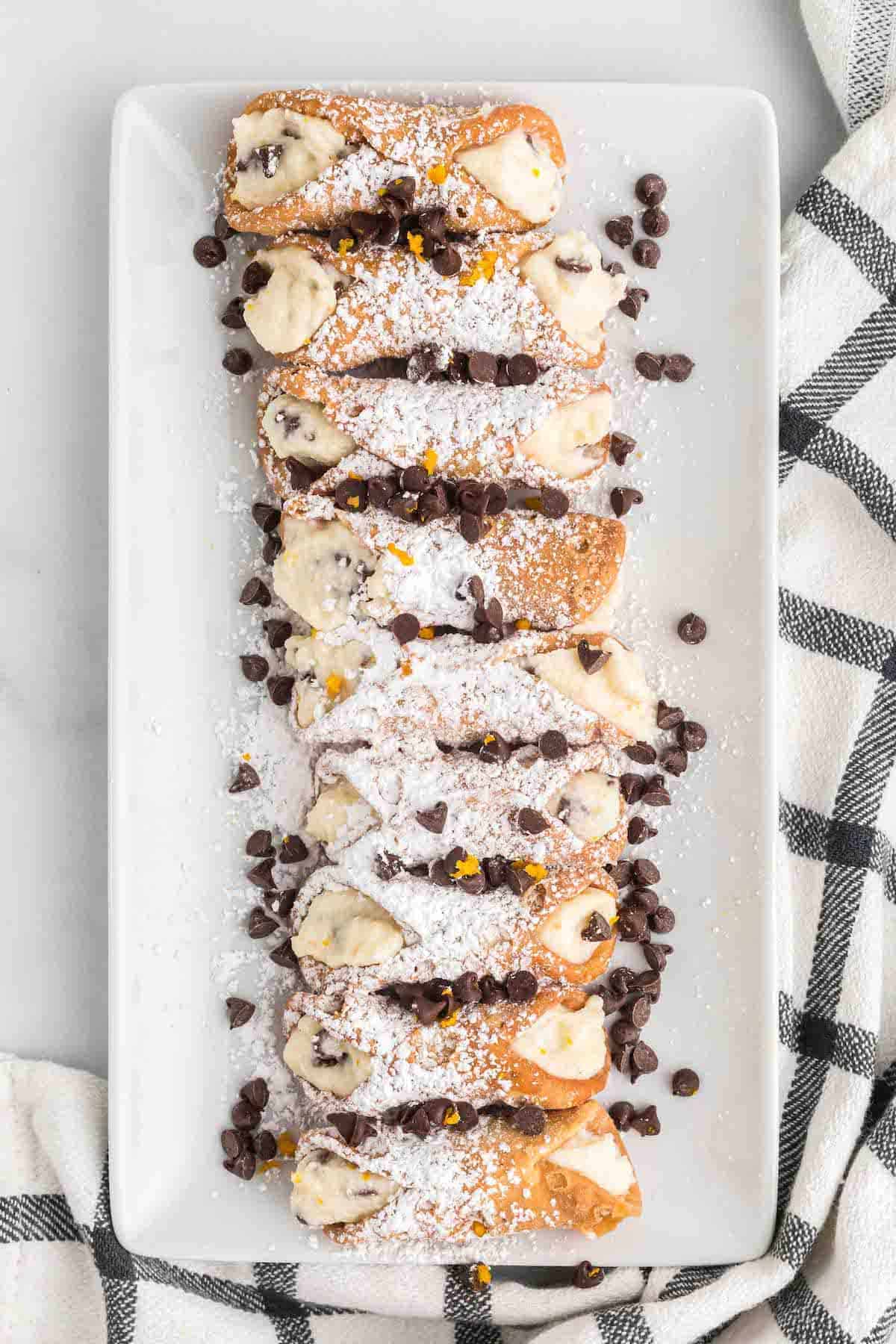 white tray with cannolis and topped with powdered sugar and chocolate chips