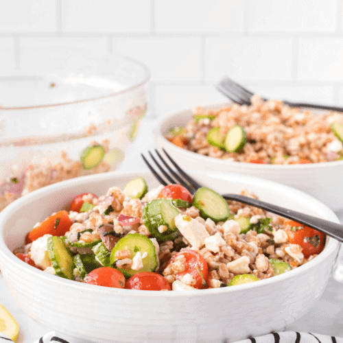 two white bowls of Mediterranean Farro salad with black forks on top
