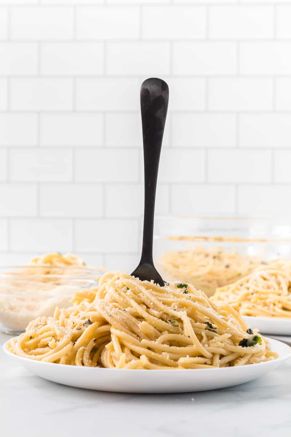 white plate with spaghetti aglio e olio and black fork sticking inside the center