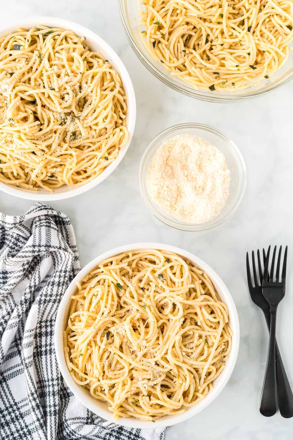 three bowls of spaghetti aglio e olio with black forks resting to the side 