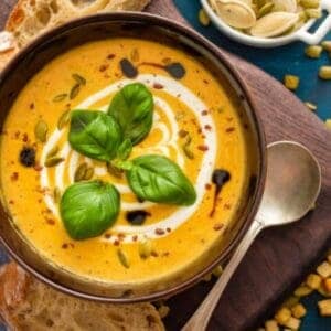 pumpkin soup with basil garnish resting on a wooden cutting board with a slice of rustic bread beside it
