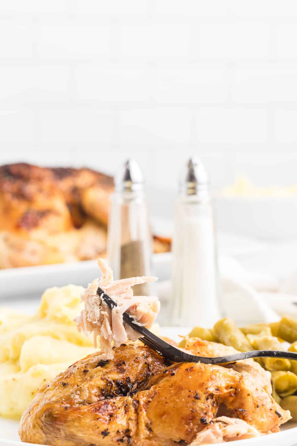 white plate of roasted italian chicken with a black fork and salt and pepper shakers in the background