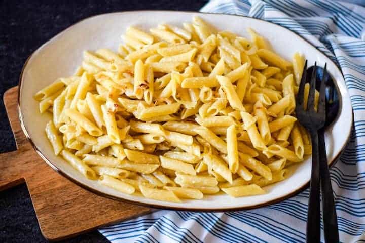 finished pasta on a white platter with black serving utensils