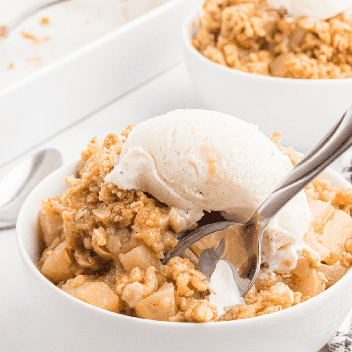 pear crisp in a white bowl with a scoop of ice cream and a serving spoon.