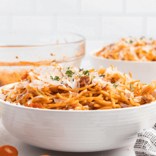 large white bowl of the ninja foodi spaghetti with shredded Parmesan cheese & fresh basil on top