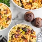 large serving bowl and two white bowls with the finished Mediterranean pasta salad.
