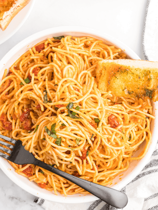 creamy sun-dried tomato pasta in a large white bowl with a piece of garlic bread to the side