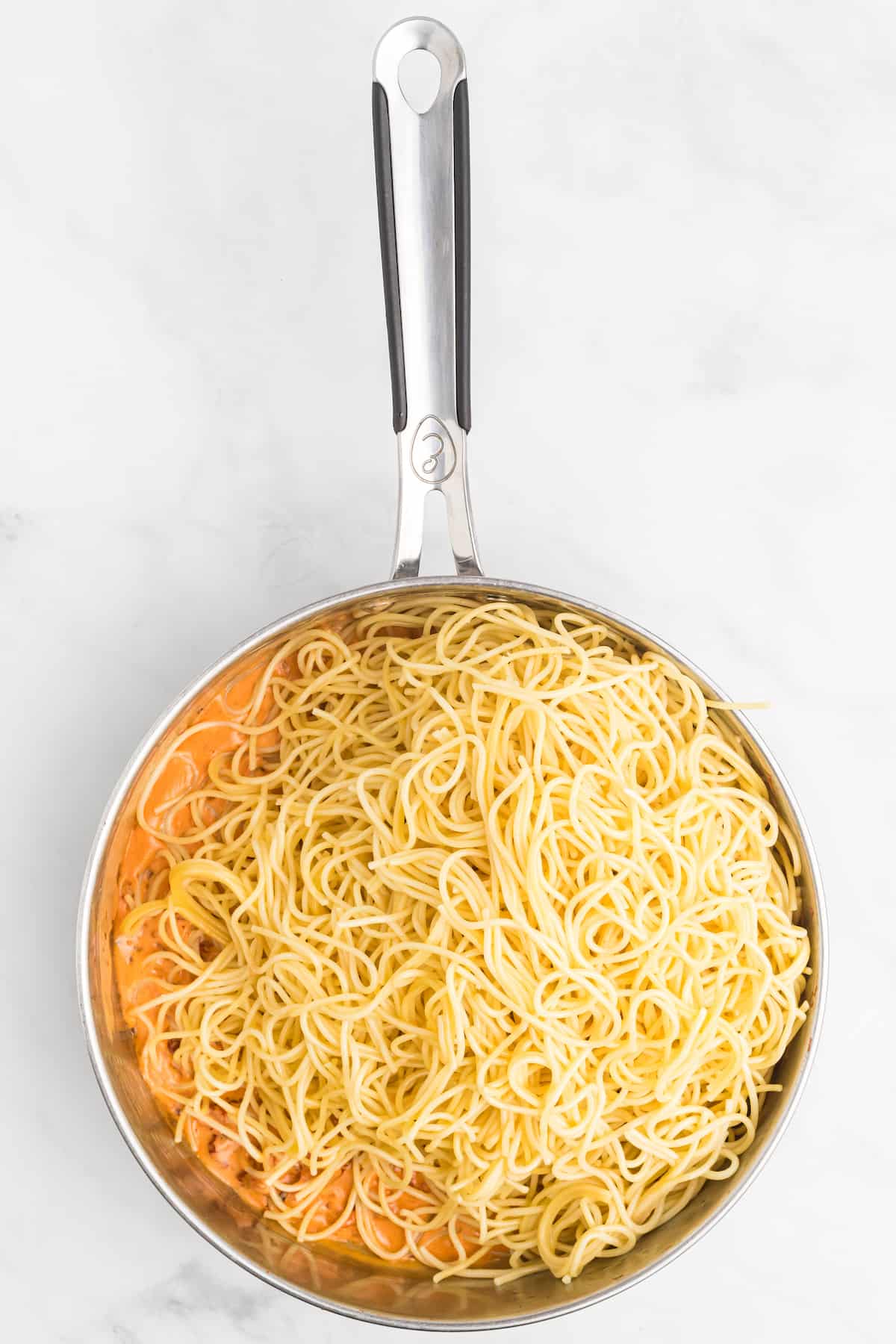 spaghetti noodles on top of the tomato cream sauce in a large skillet