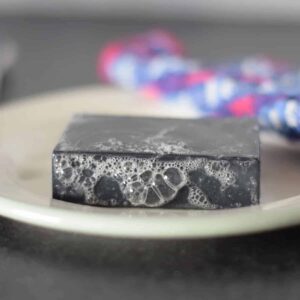 charcoal soap bar on a white plate with suds