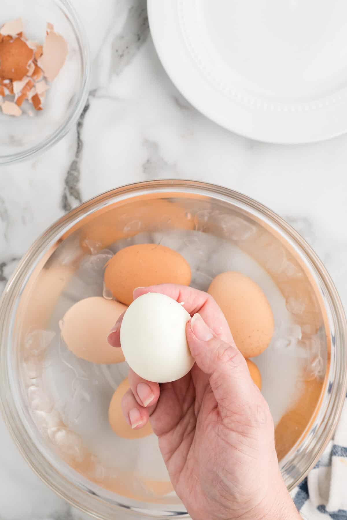 holding a peeled hard boiled egg in hand over the ice water bath. 