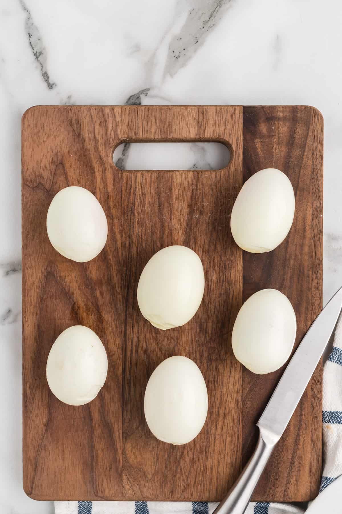 fresh peeled hard boiled eggs on a wooden cutting board with a knife to the side. 