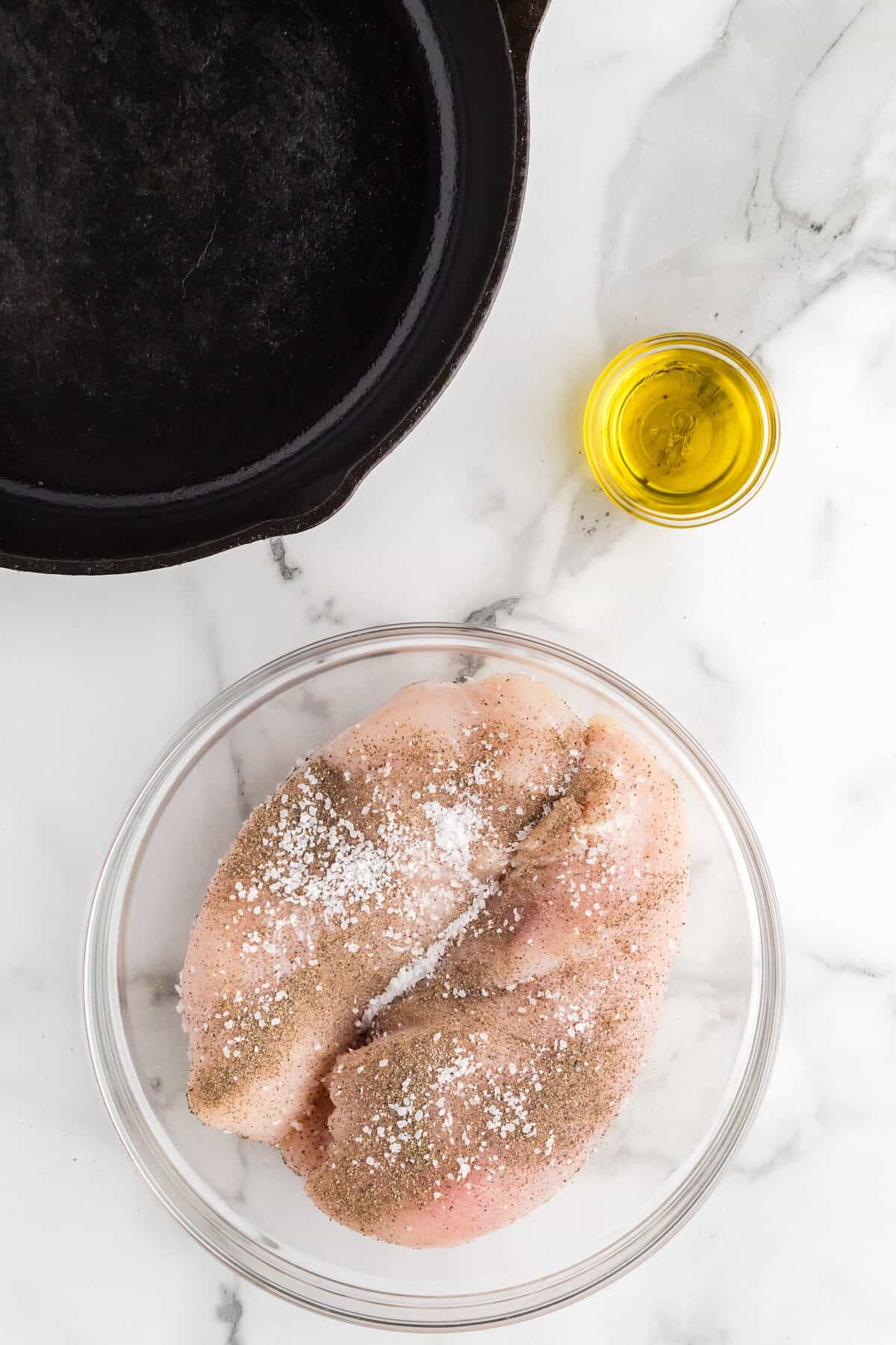 chicken breasts seasoned with salt and pepper in a large glass bowl.