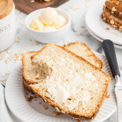 slices of honey oat bread on a small white plate with butter spread over top.