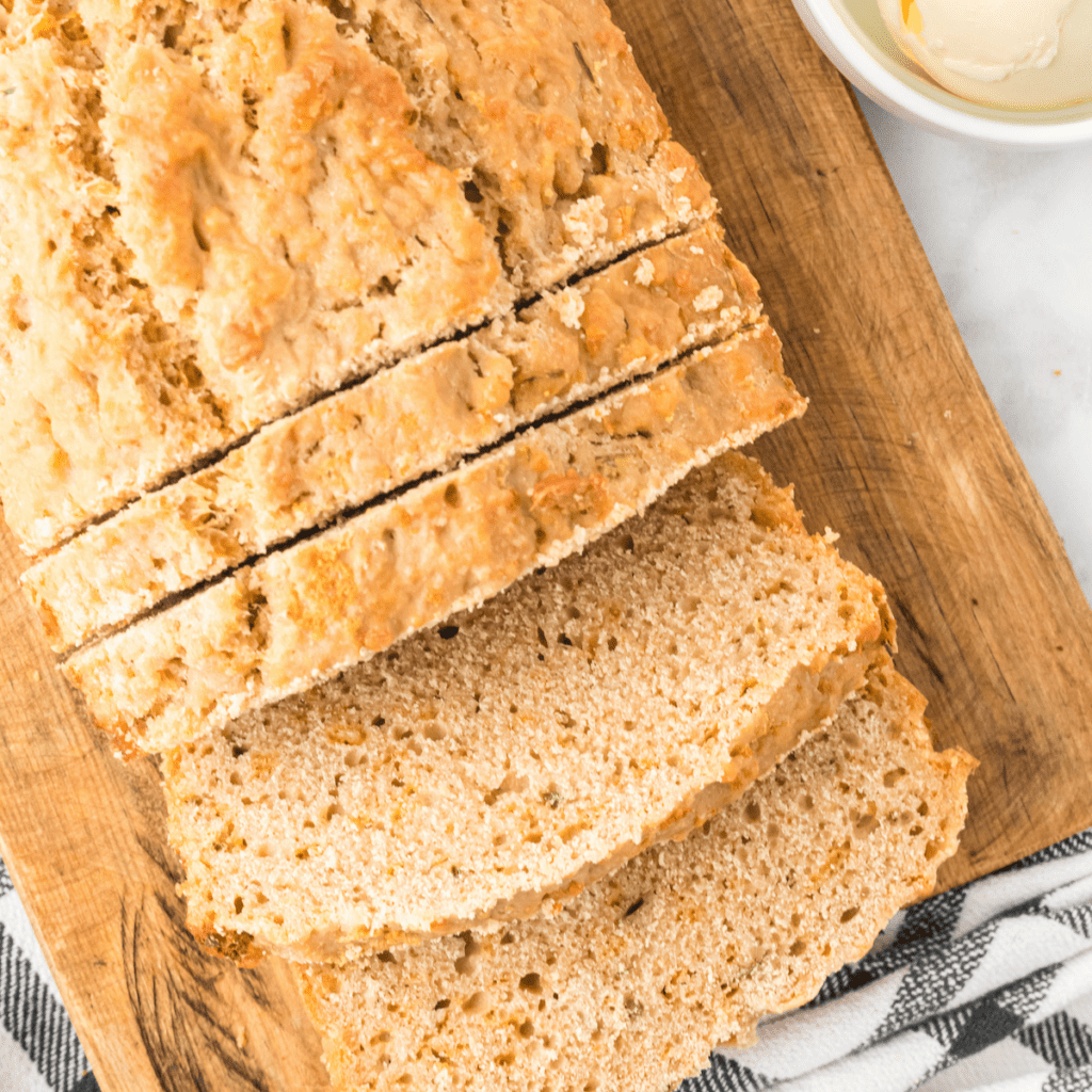 loaf of cheddar beer bread on a wooden board with a few slices and butter in a small bowl