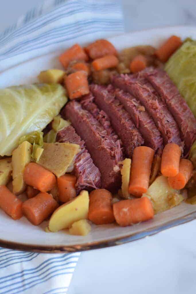 white platter layered with corned beef and cabbage, potatoes and carrots